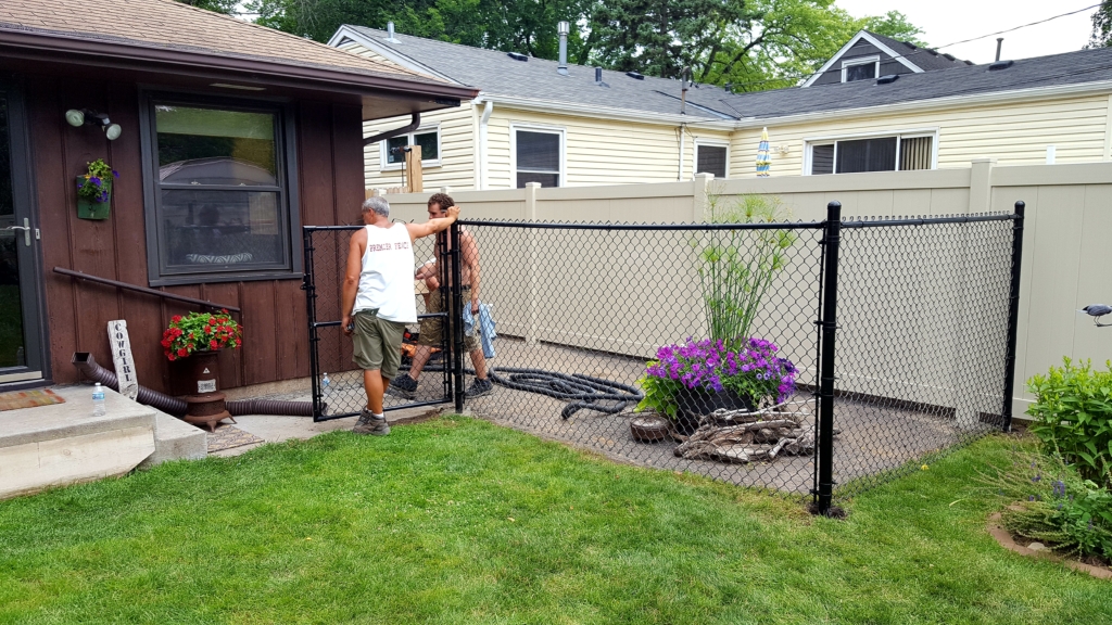 Premier Fence installers building a vinyl privacy fence and a black vinyl coated chain link fence on a Summer day